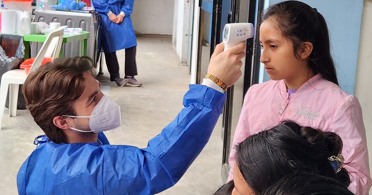 University of Delaware alum Alec Mackinnon, who majored in medical diagnostics with a pre-physician assistant, concentration, takes the temperature of a patient using a forehead scanner during intake at a MEDLIFE clinic outside Lima.