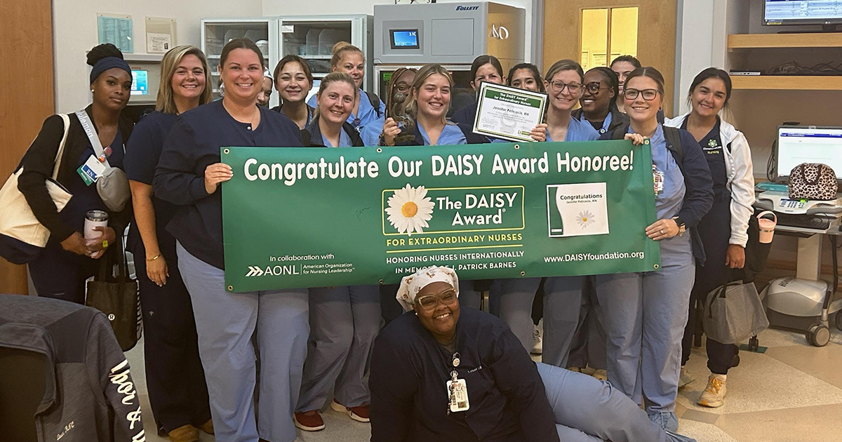 University of Delaware alumna Jennifer Peticacis poses for a photo with her ChristianaCare colleagues, holding up a green banner congratuliating her on winning the DAISY Award, which recognizes nurses for their compassionate care.