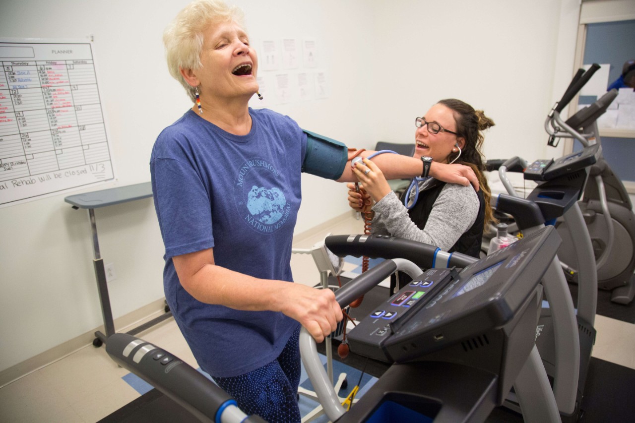 Student working with a patient, taking their vitals while on a cardio exercise machine
