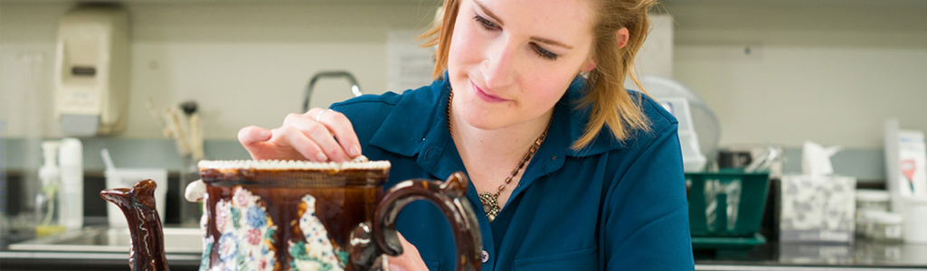 Close up view of a female art student working on a piece of pottery.