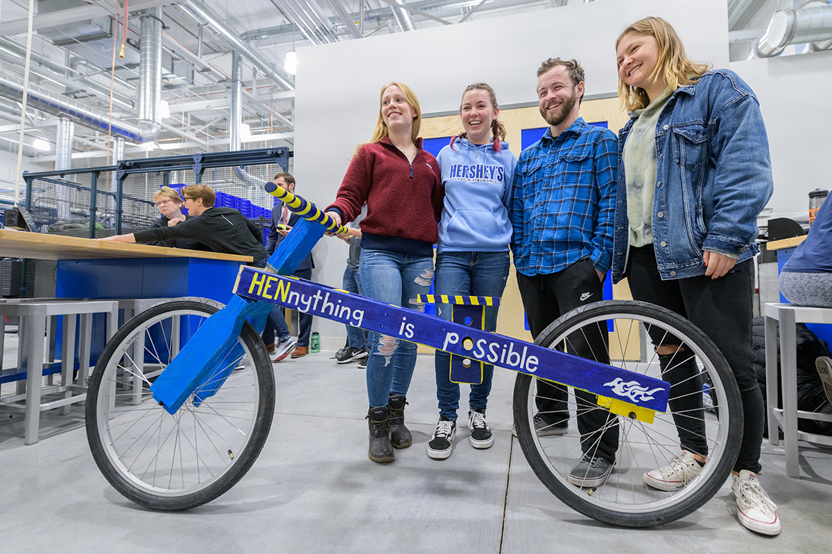 Mechanical engineering students stand with the wooden frame bicycle they built in a hands-on design class.