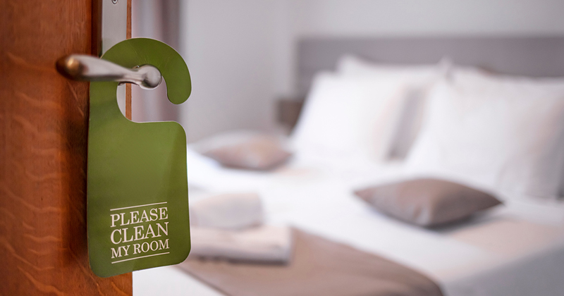 A door opens into a clean hotel room with a green sign on it that says 