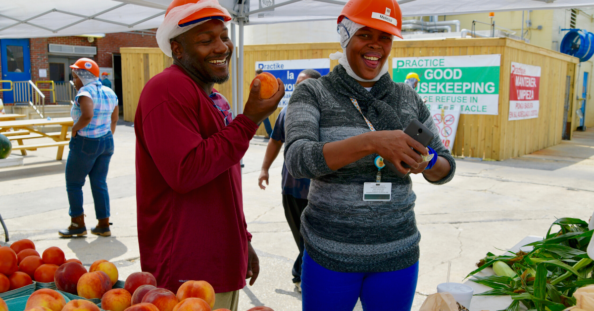 Two Perdue employees enjoy fresh fruit on a hot summer day at a worksite farmer's market.