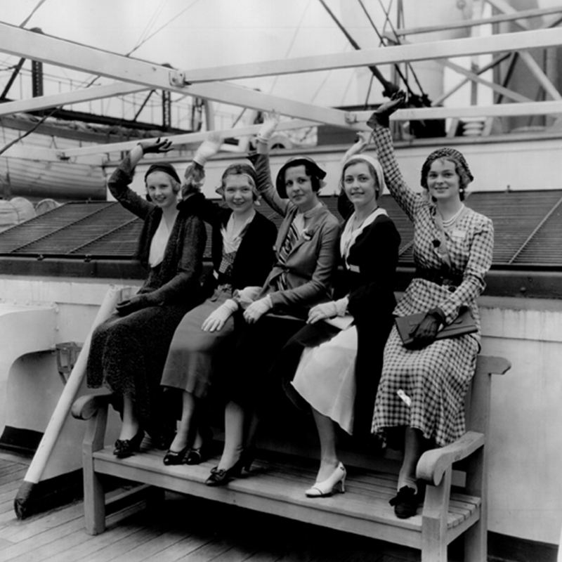 A black and white historic images of five women waving on a ship.