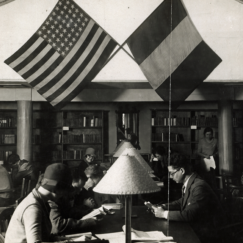 A black and white historic image of two students studying at a desk with the American and French flags above.
