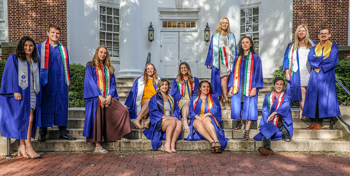 UD World Scholars stand and sit for a photo in their graduation regalia.