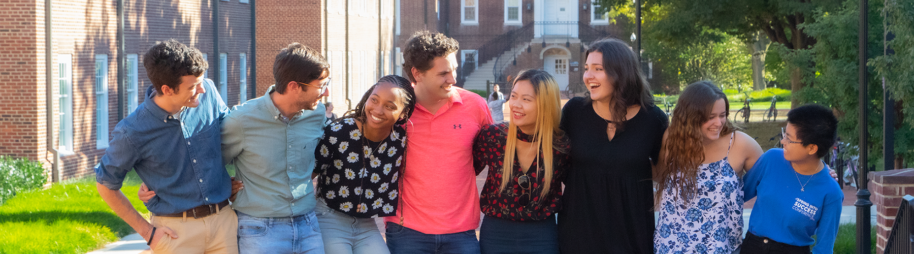 A group of diverse students with arms around their shoulders, laughing and smiling.