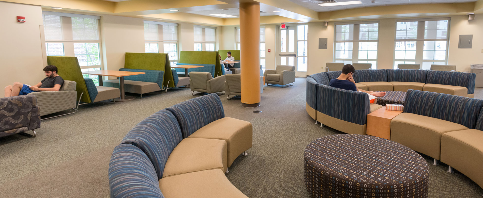 Students relaxing and studying in lounge with comfortable chairs and a curved, modular sofa