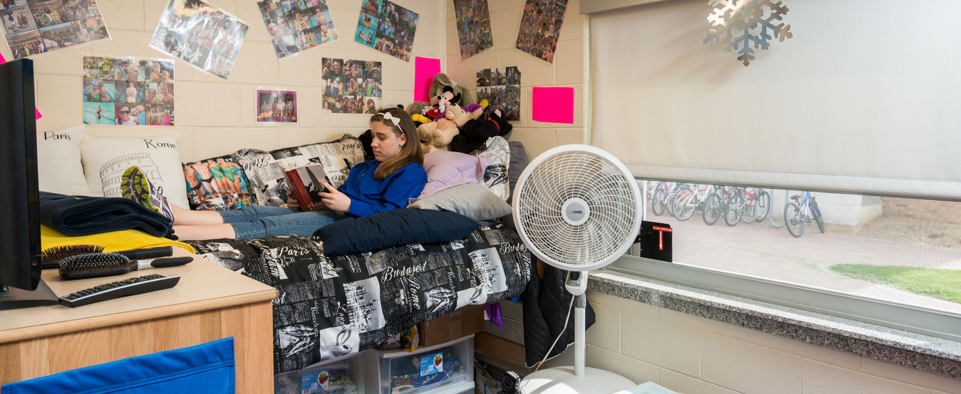 A student lays on their bed in residence hall, reading a book