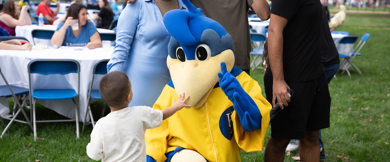 Small child interacts with YoUDee at the 2023 Parents and Family Weekend Welcome Reception
