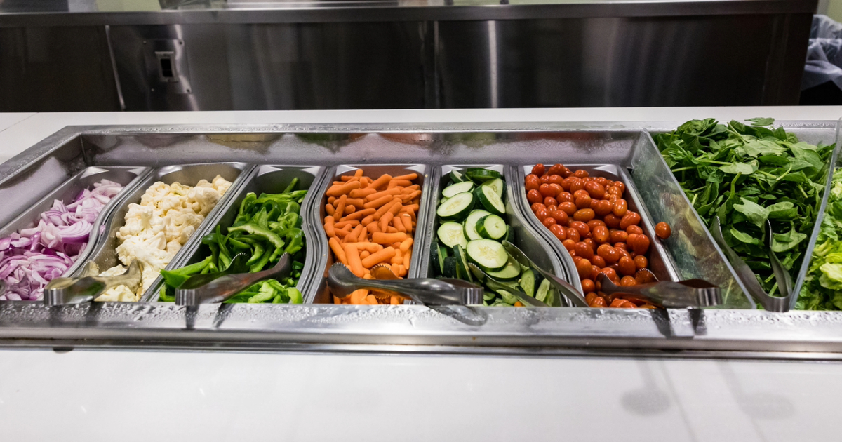 Dining hall salad bar of onions, carrots, cucumbers, tomatoes, spinach and more