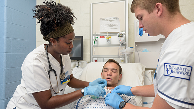 Undergraduate nursing students Cory Haaf, Jennifer Shellenberger, and Jerelene Thorpe perform various simulated tracheostomy related tasks on "patient" Robert Tilley who's wearing a SimUTrach: a high-fidelity tracheostomy overlay. The SimUTrach device was developed as a senior class project in 2014 by UD students and brought to market by SimUCare, a company based out of the University of Delaware. - (Evan Krape / University of Delaware)