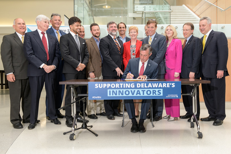 UD President Dennis Assanis (far right) and other dignitaries watch as Delaware Gov. John Carney signs the Angel Investor Job Creation and Innovation Act into law on UD’s STAR Campus.