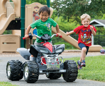 Two children, one using the GoBabyGo car and one on foot interact and play together