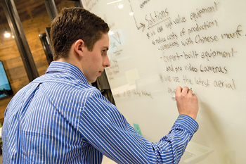 A student writing out his project description on glass board