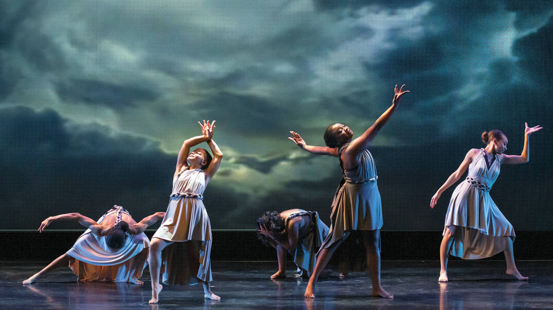 A scene from "Suite Blackness," where dancers are on stage in various poses with a stormy sky background.