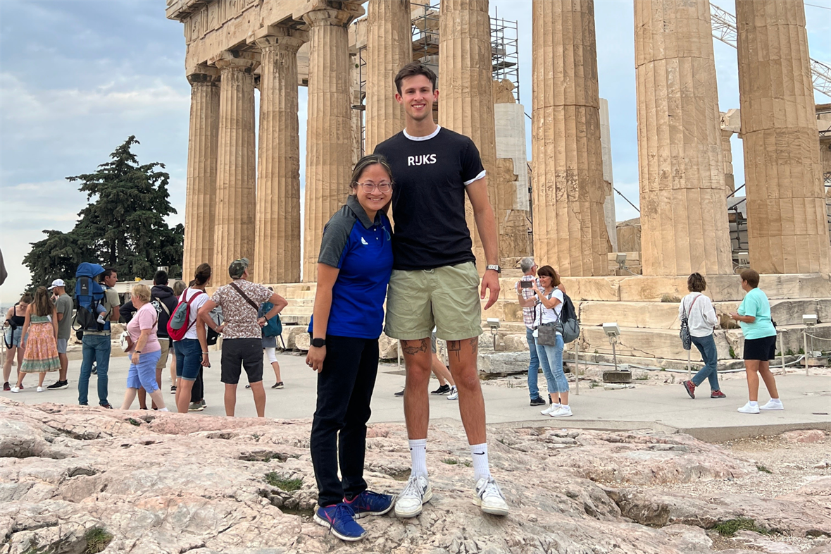 SNF Ithaca Student Leaders Jenna and Simon in Athens for the iMEdD International Journalism Forum in 2023 SNF Ithaca Student Leaders Jenna DeMaio and Simon Brand stand side-by-side smiling while on a tour of the Acropolis in Athens, Greece. Groups of other tourists and a portion of the ancient ruins are visible behind them in the background.
