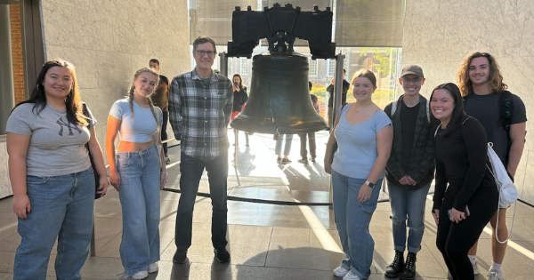 Honors UAPP110 Philadelphia enrichment trip Six adults standing and smiling in front of the Liberty Bell in Philadelphia