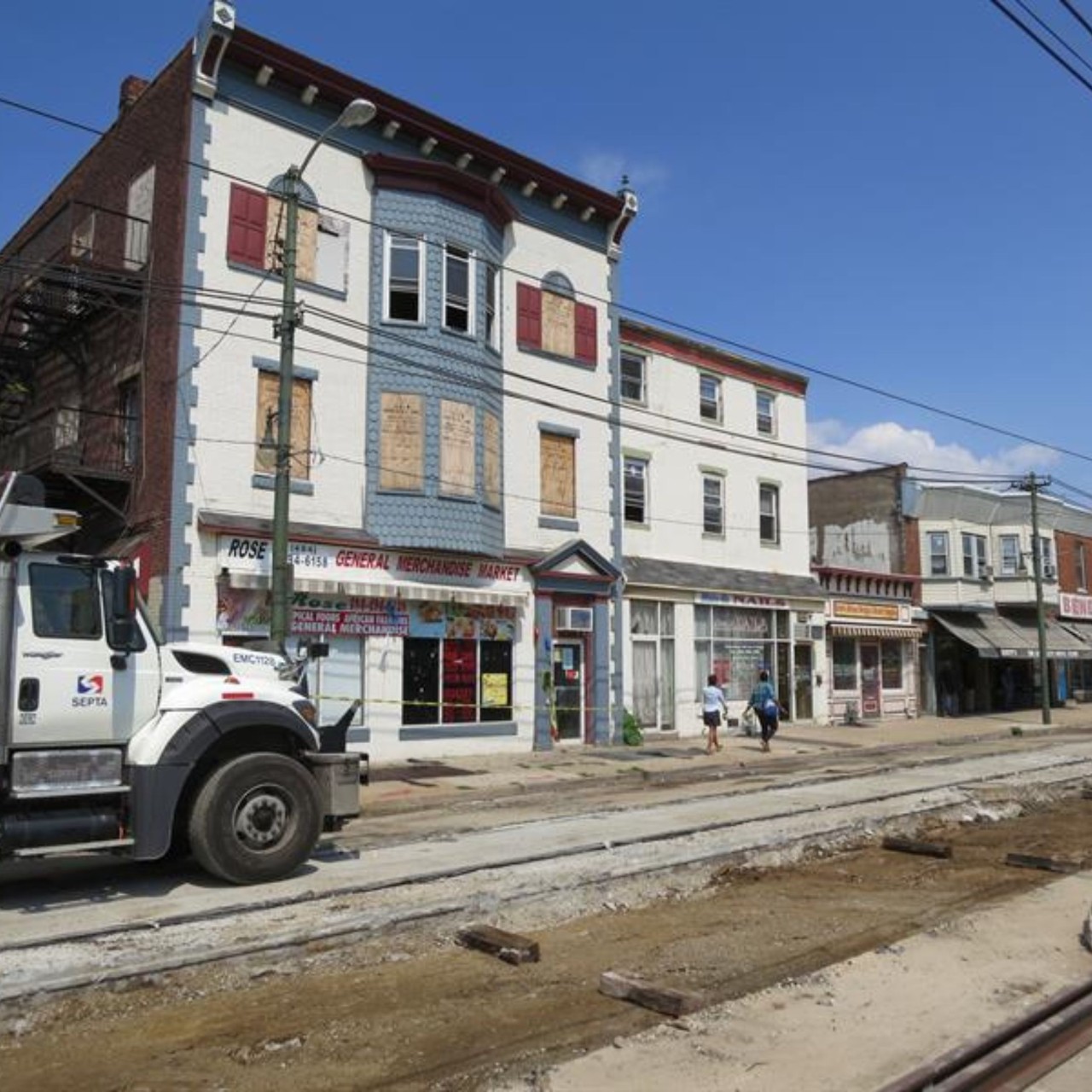 Photo of historic row buildings with boarded up windows and doors in Darby, Pennsylvania. The street is torn up in the foregorund and a constructrion vehicle is slightly visible in the lower left corner.