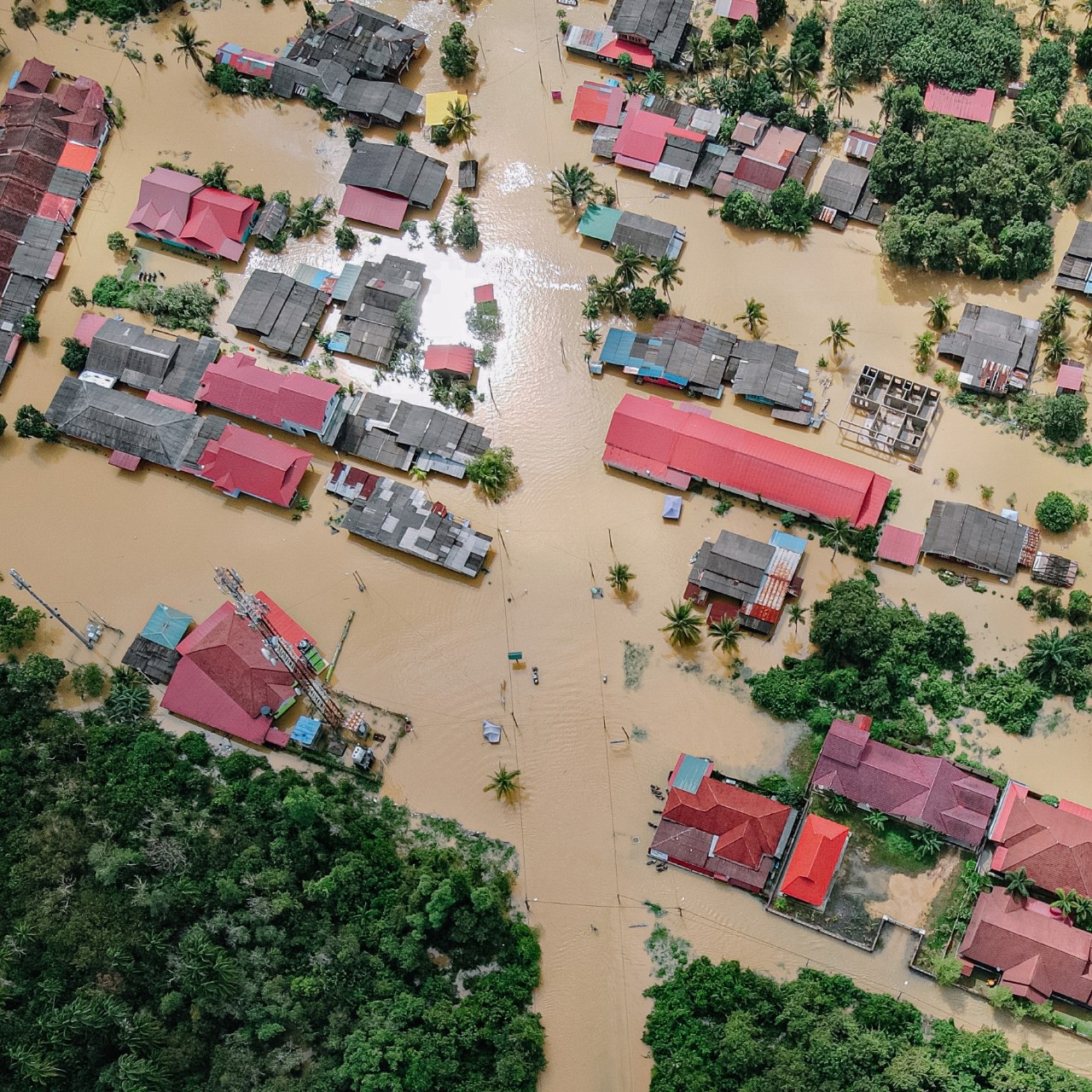 Aerial photo of the muddy, flooded streets of a neighorbood with only roofs visible in the aftermath of a natural disaster.