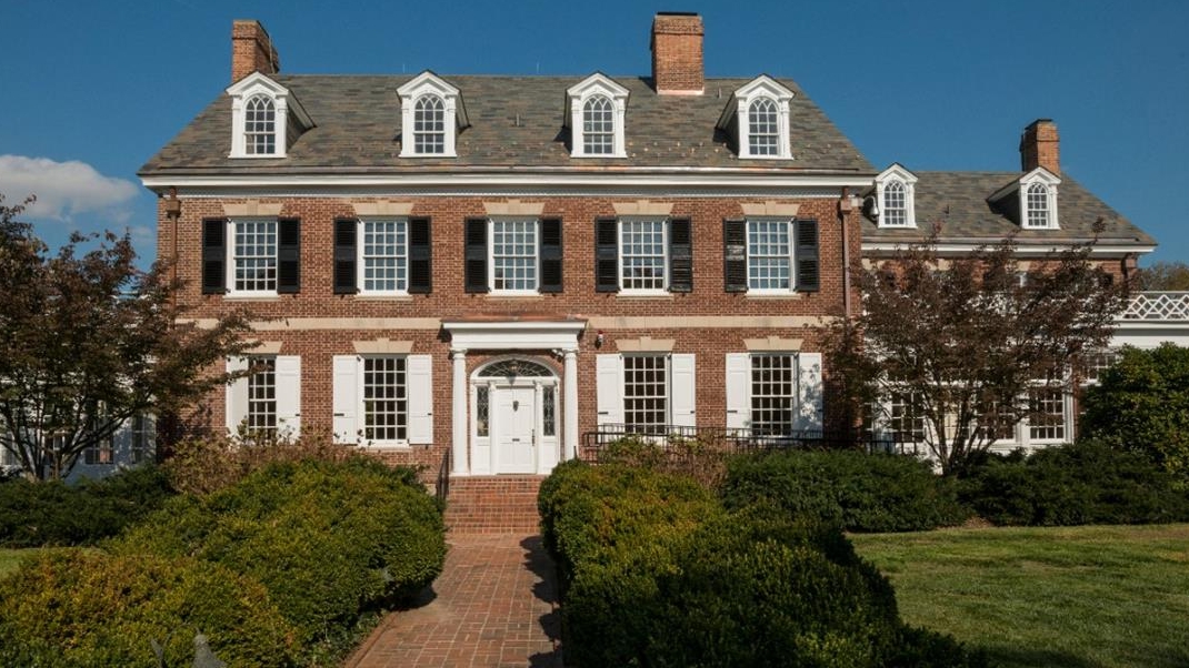 Photo of the Biden Institute building exterior, consisting of a large brick house framed by greenery and a bright blue sky