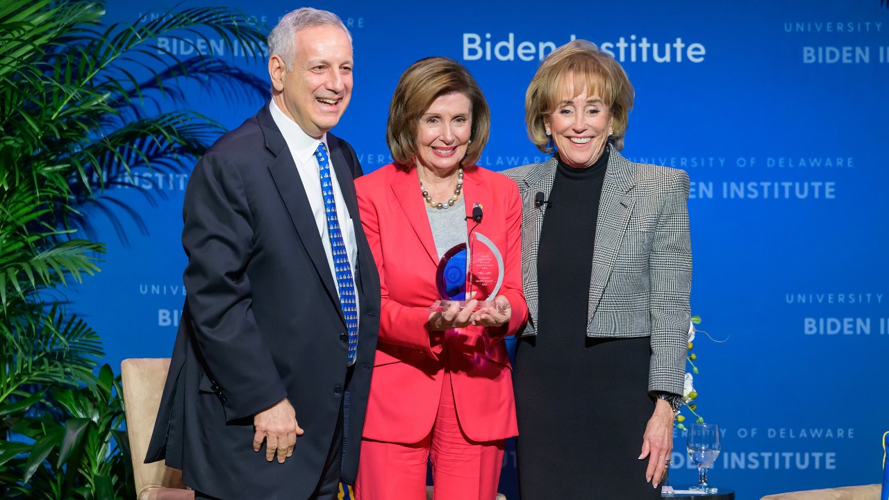 Photo of UD President Dennis Assanis, Speaker Emerita Nancy Pelosi and Biden Institute Chair Valerie Biden Owens stand side-by-side smiling and waving
