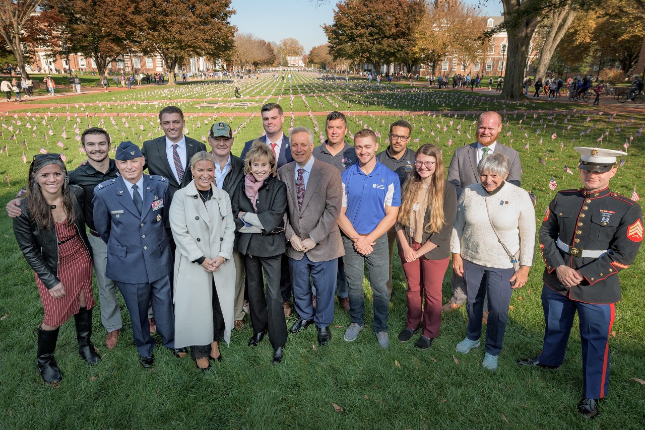 Photo of Blue Hen Veterans and UD community members gather with special guests in front of the Flags on the Green display on campus