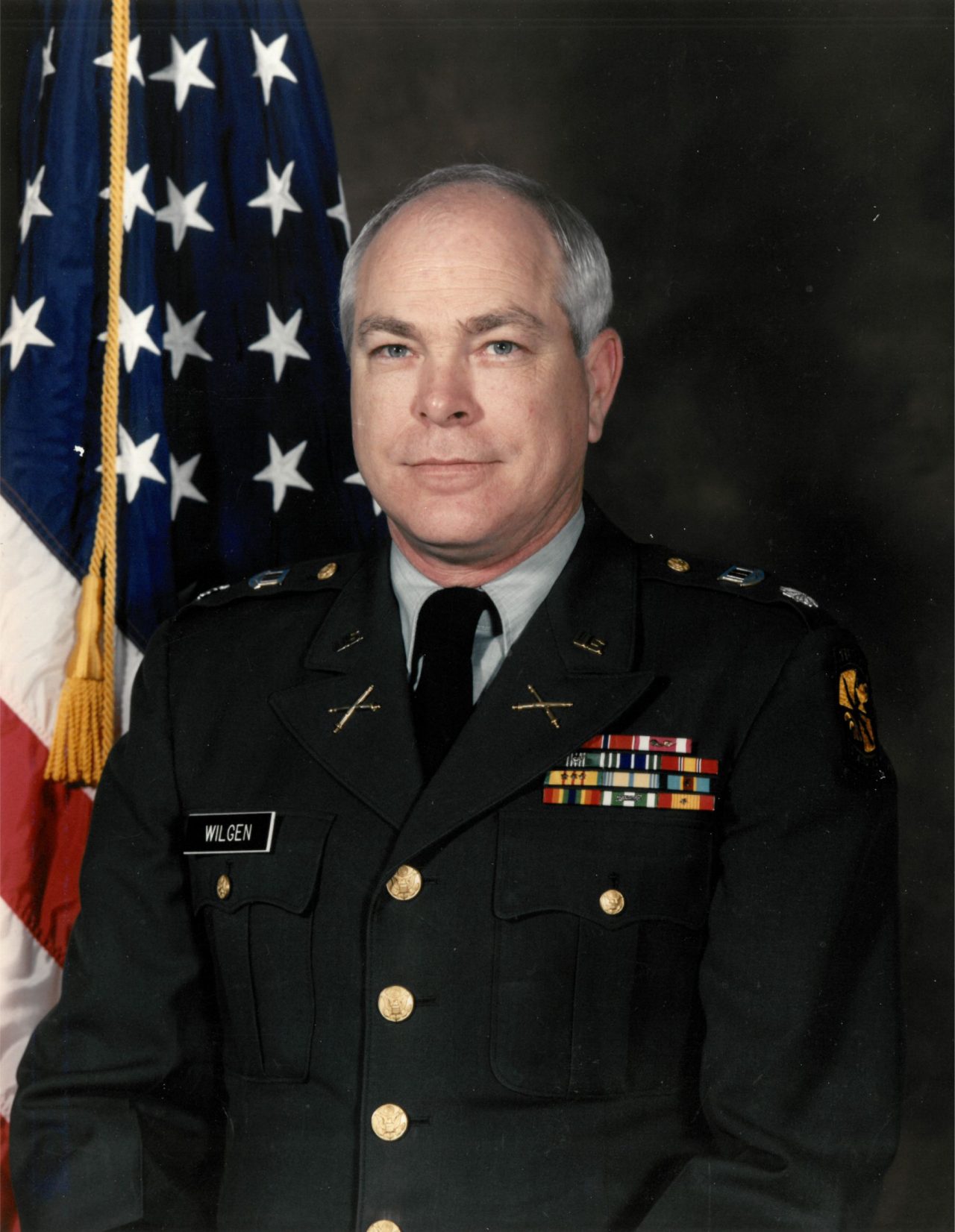 Portrait photo of Lt. Col. Michael C. Wilgen in full military dress in front of a dark background with the American Flag in partial view on the left side