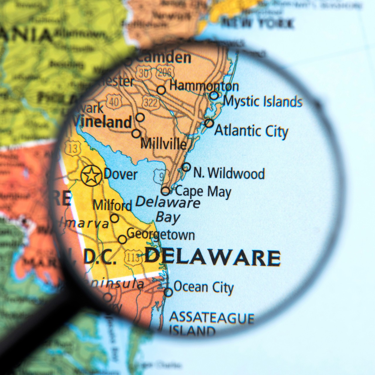 Photo illustration of a black magnifying glass hovering over a multicolored map of the east coast, focused on Delaware