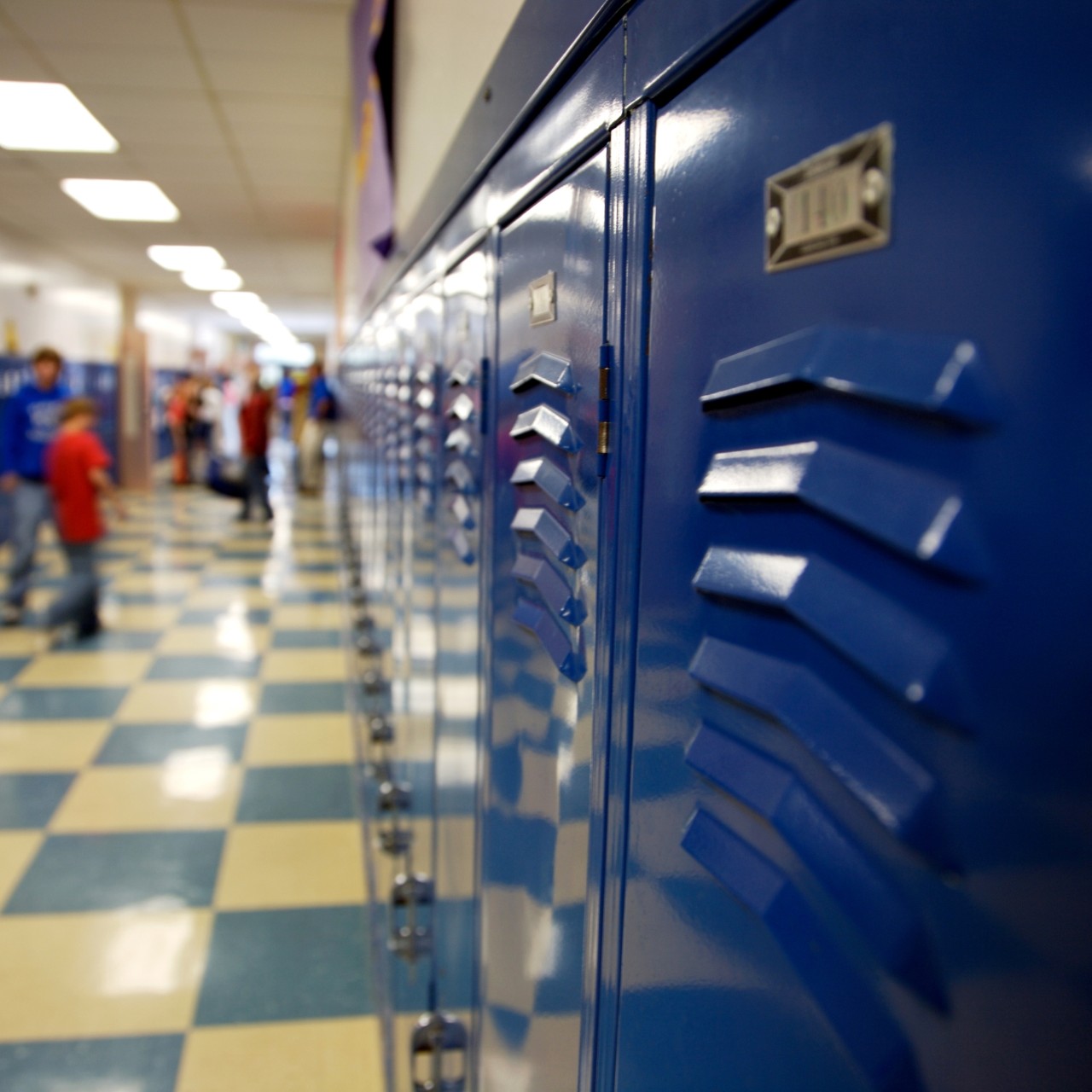Close-up photo of a row of blue lockers in a brightly lit school hallway with yellow and green checkered floors