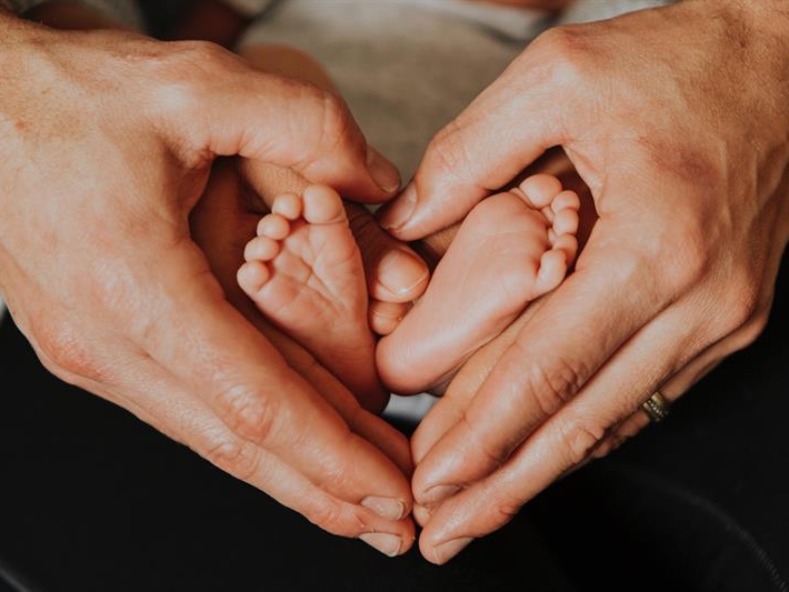 Photo of a set of adult hands holding a pair of baby feet in the shape of a heart