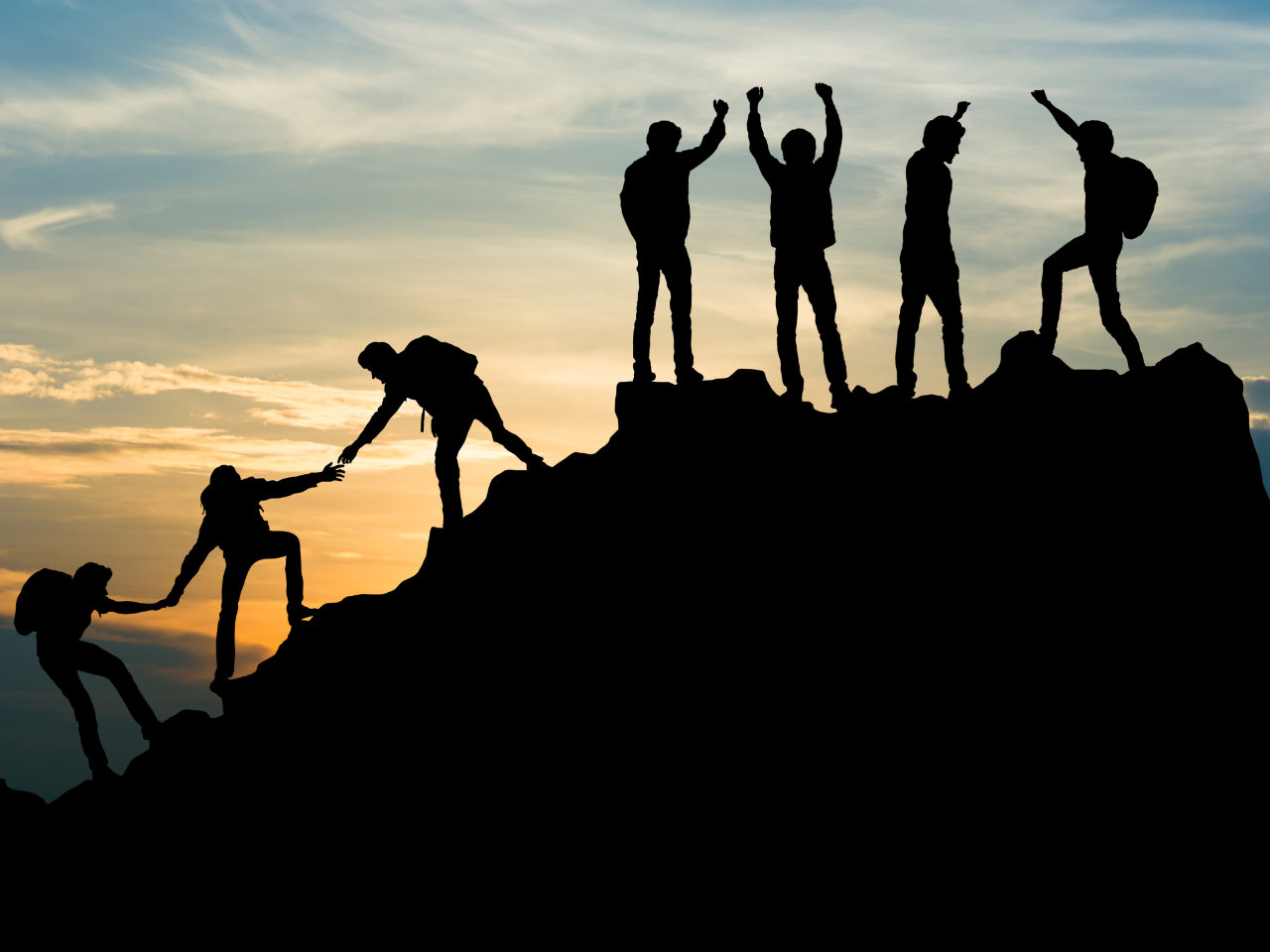 Photo of the dark silhouette of a mountain top against the sky at sunset while the silhouettes of eight human figures are seen helping each other up to the top