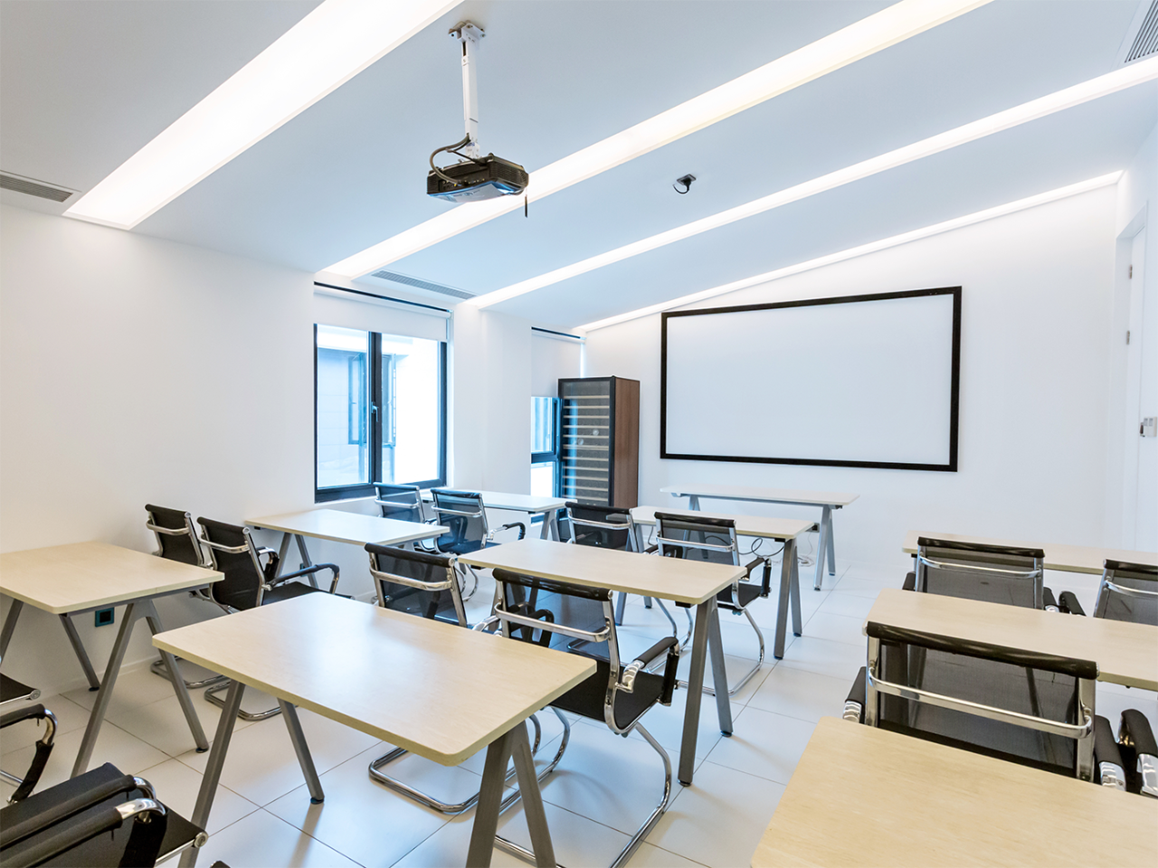 Photo of an empty training classroom, complete with large desks and chairs, a projector and a large monitor in the background