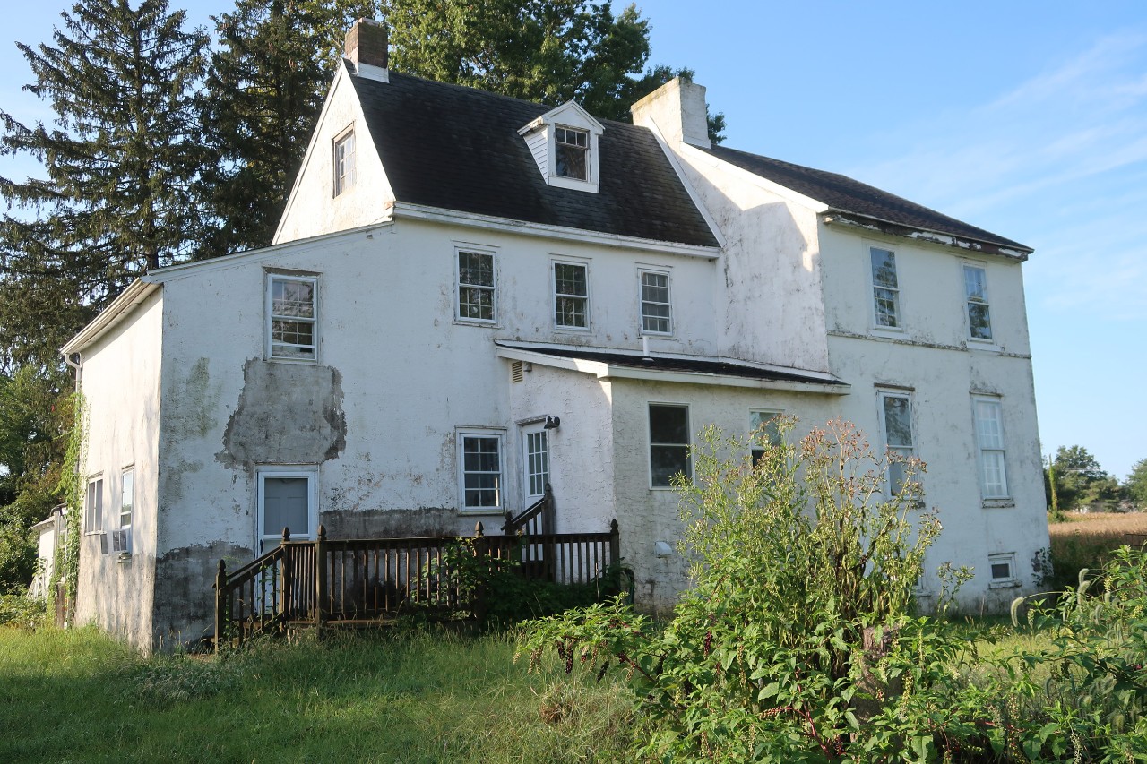 Photo of the exterior of a white-colored, historic property in Delaware surrounded by greenery and a blue sky