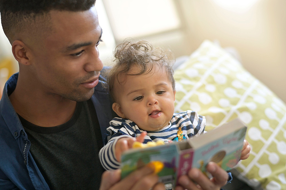 Black father holding his infant daughter as they look at a picture book together