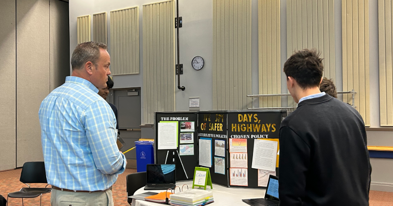 A photo of two students and a judge participating in the Project Citizen 2024 showcase