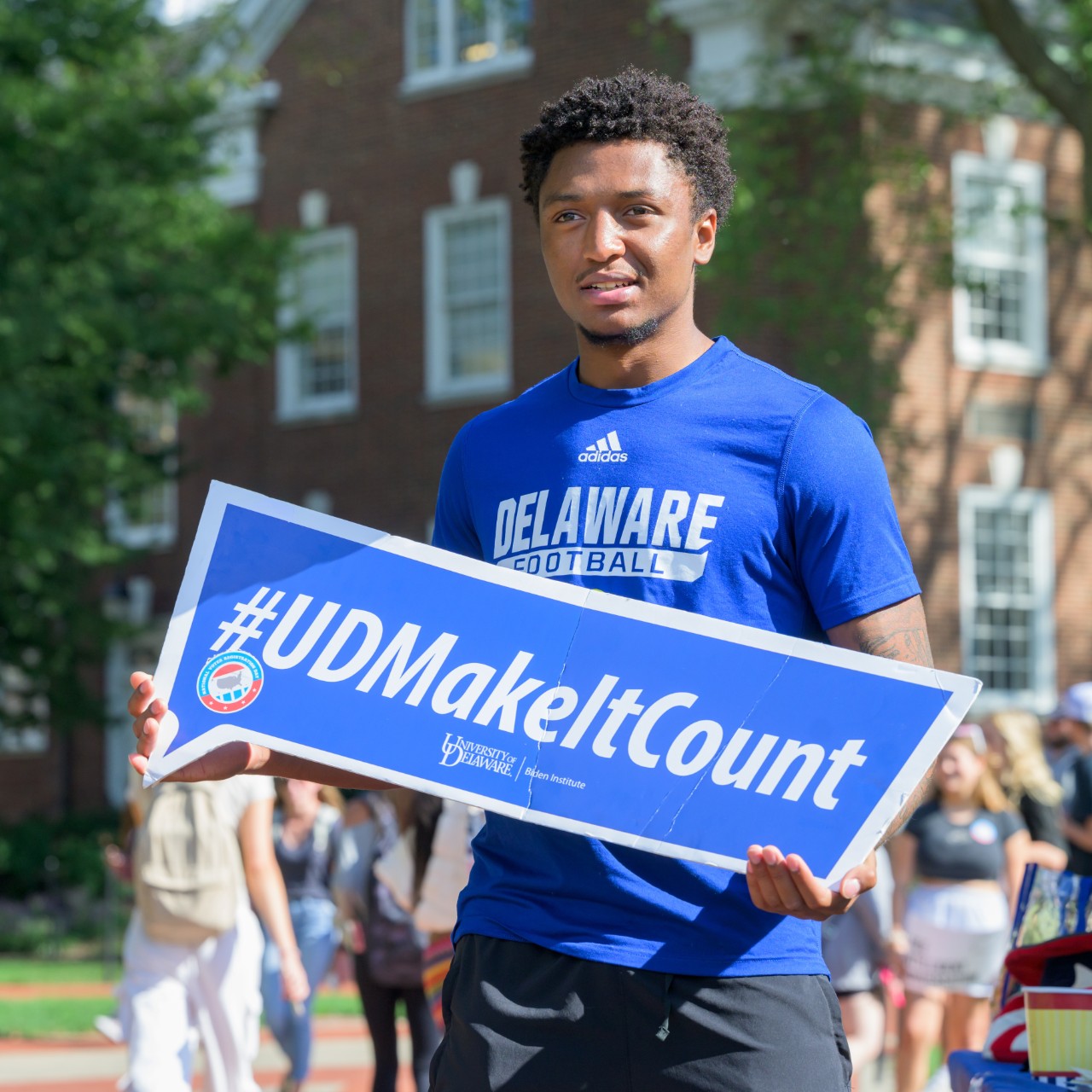 Student holding #UDMakeItCount Sign on Campus Green