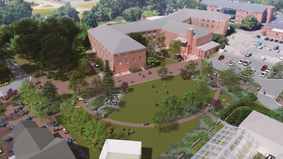 A view of the proposed site from the air, featuring a large green lawn area, benches, a restroom facility, brick pathways and greenery.