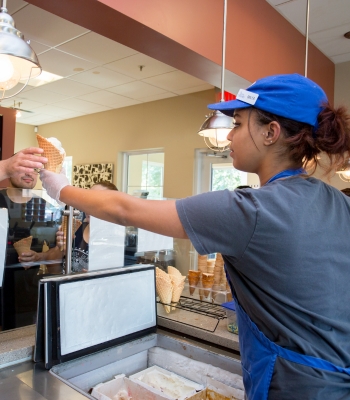 A student handing freshly-scooped ice cream to a customer.