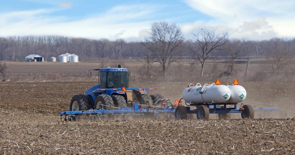A blue tractor spraying / applying nutrients to a field.