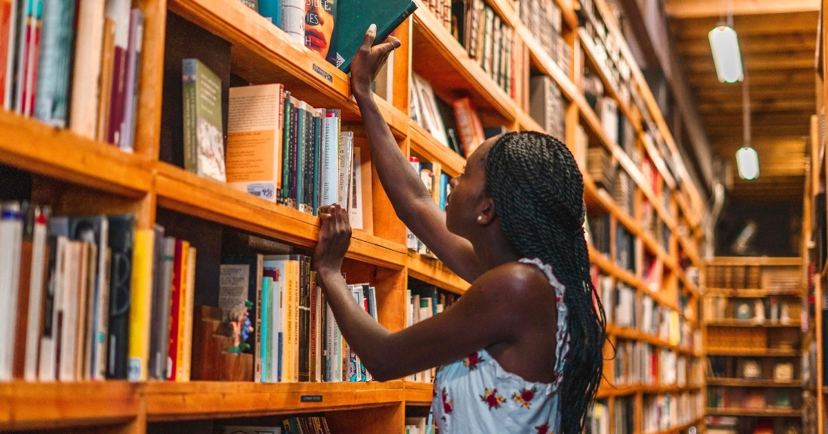 A woman reaching for a book in a library.