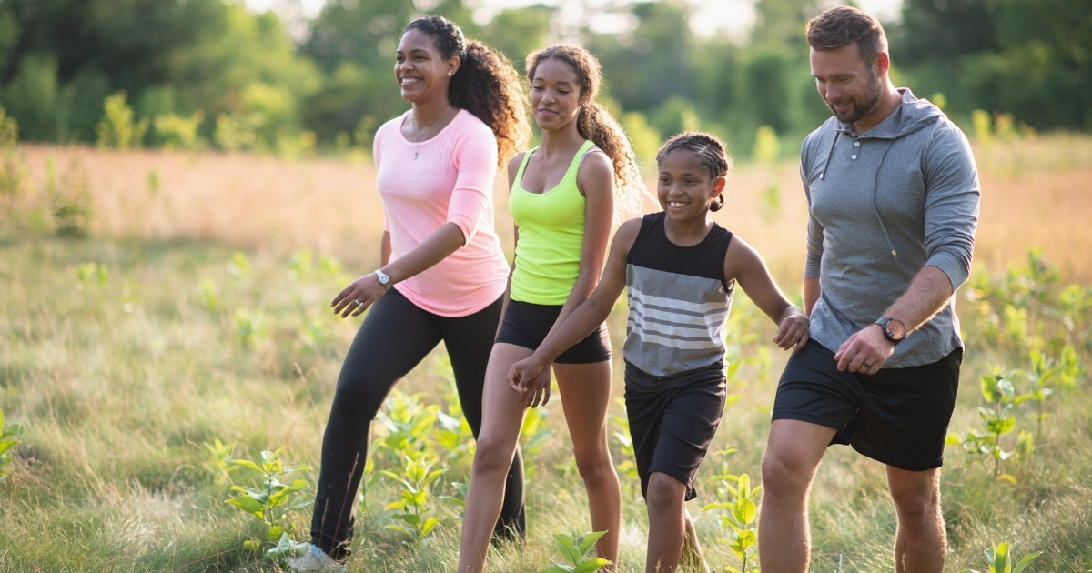 A family with two young teen children on a hike in a meadow near the woods.