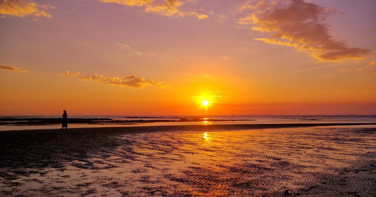 A person walking on the beach at sunset, contemplating.