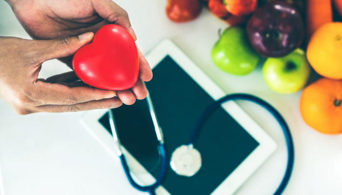 Hands holding a heart shaped toy near fresh fruit and stethoscope