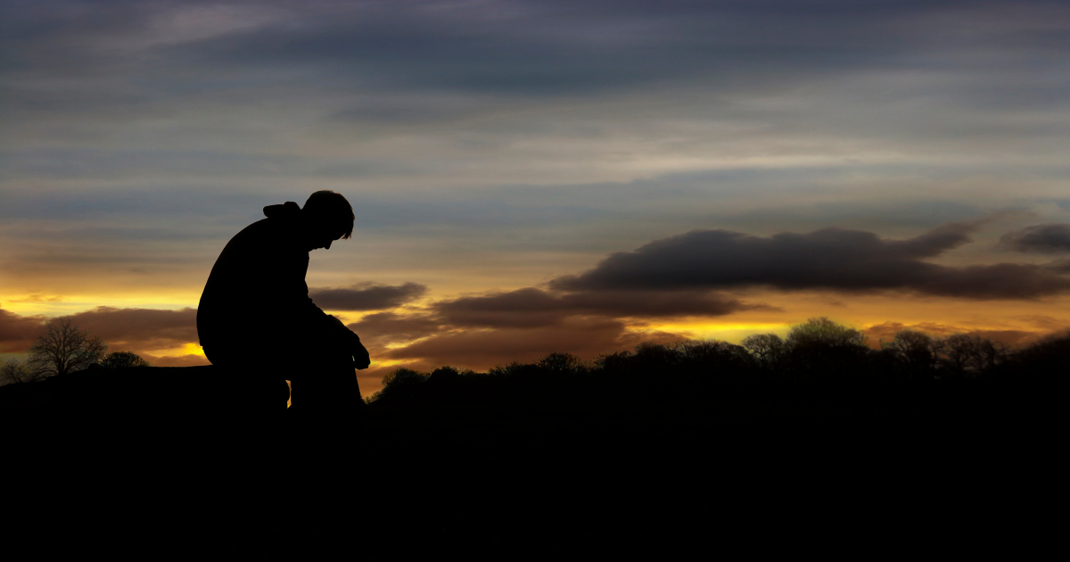 A grieving man silhouetted against a rural sunset.
