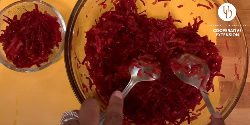 Two hands stir a bowl of beet and apple salad together.