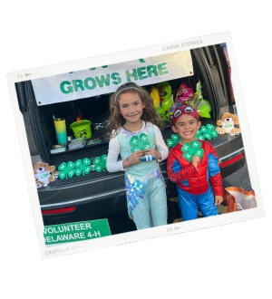 Two children in Halloween costumes standing in front of their opened truck for Truck or Treat with 4-H