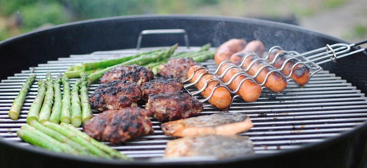 A grill with asparagus, hamburgers and hotdogs.