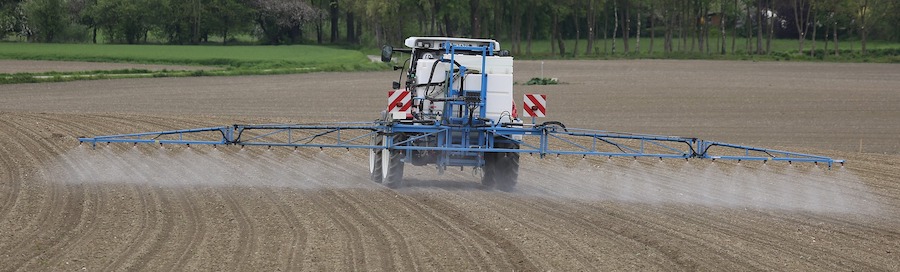 A farmer on a tractor, applying pesticides to a field.