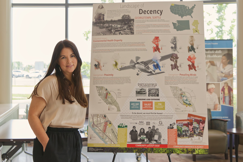 Undergraduate student stands next to a poster displaying her landscape architecture plan.